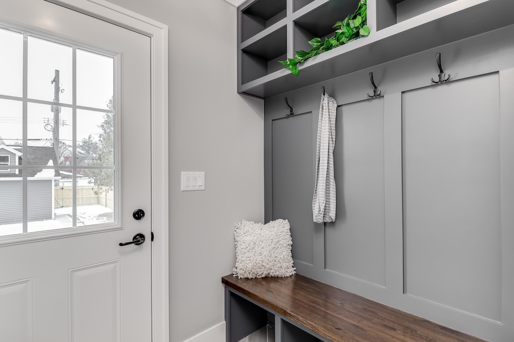 A gray mudroom with bench seating, coat hooks, and storage above.